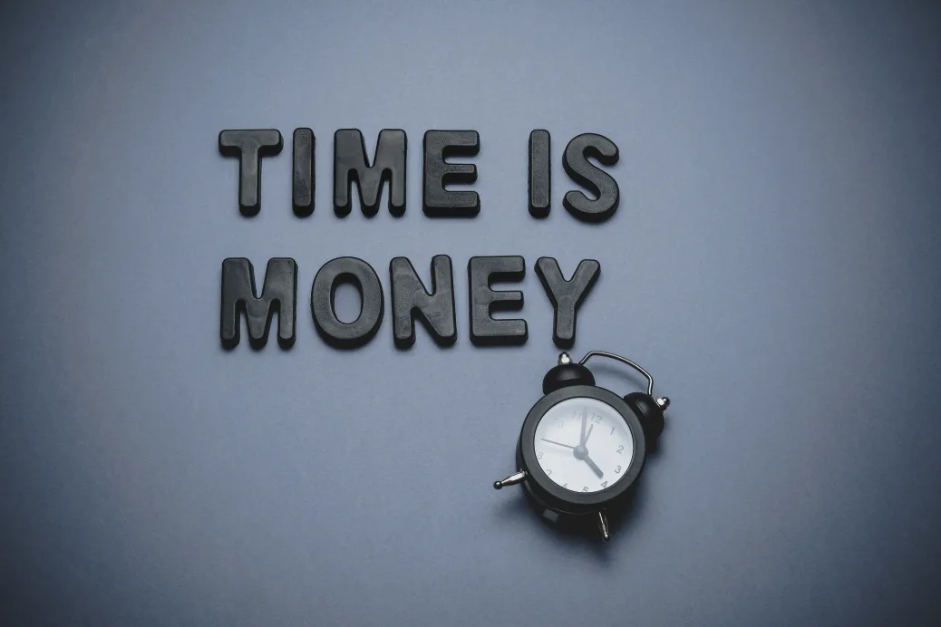 photo of a retro analog alarm clock with two bells on top next to wording that reads, "time is money" on a greyish background